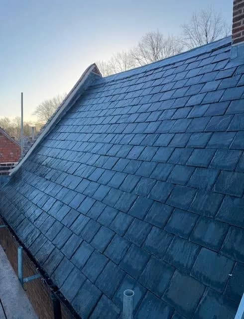The completed slate roof photographed in low winter sun, the courses running evenly down the slope to the eaves with the lead ridge along the top and the gable verge picked out against a pale sky.