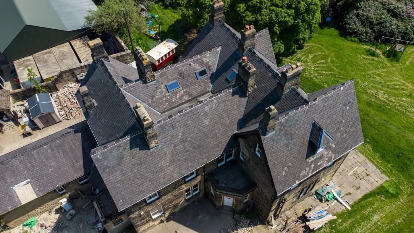 Overhead view of the finished roof: uniform newly laid natural slate across the main pitches, crisp new lead work in the valleys and freshly fitted rooflights, with the stone chimney stacks retained.