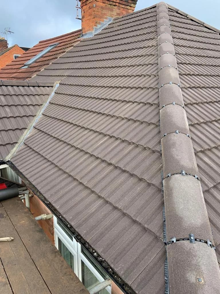 Close-up of a freshly tiled brown interlocking roof with a mechanically clipped ridge running down a hip, above a bay window.