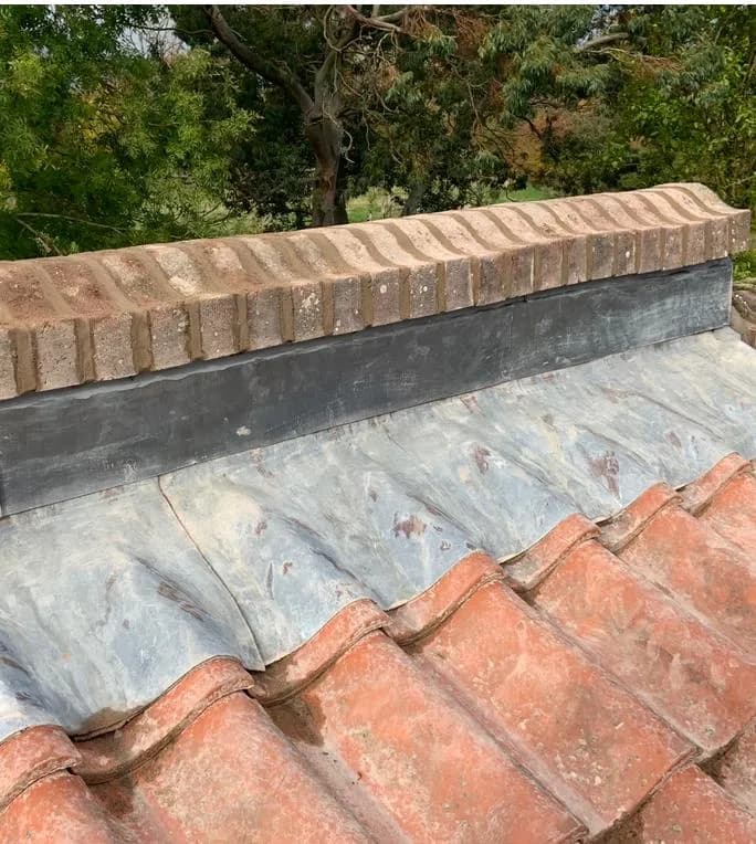 A rebuilt roof verge with a clean coping and fresh grey lead flashing over tidy clay pantiles, after the work was completed.